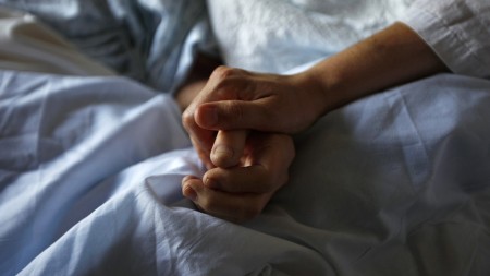 A woman holds the hand of her mother who is dying from cancer during her final hours at a palliative care hospital in Winnipeg