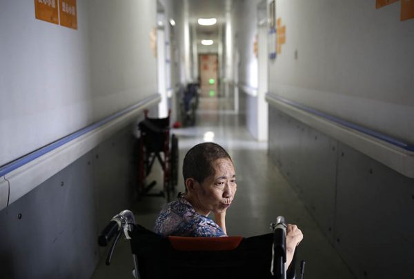 A woman sits in a wheelchair in the hallway of Songtang Hospice, Beijing, July 19, 2016. 