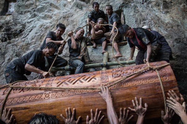 People lift the coffin of Liling Saalino to a stone grave, or Liang, during a burial ritual, or Rambu Solo ceremony, in Lemo village, Toraja, South Sulawesi, Indonesia. During the procession, people chat “Tau Tae Sengke,” which means nobody should be angry.